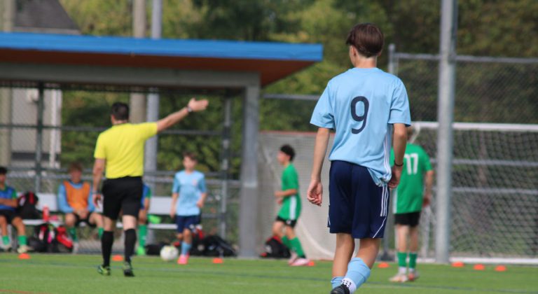 Soccer player watches a referee signal at the BC Summer Games.
